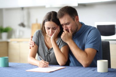 Evdeki mutfakta kağıt okuyan üzgün çift.