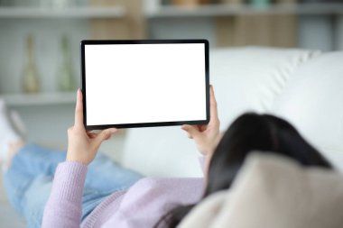 Kanepede tablet kullanan bir kadın boş ekranı evdeki kanepede yatarken gösteriyor.