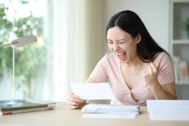Heyecanlı Asyalı kadın ödemenin bitişini kutluyor. Faturası evde bir masada duruyor.