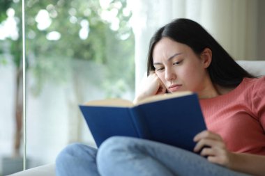 Evdeki kanepede oturmuş kitap okuyan sıkıcı Asyalı kadın.