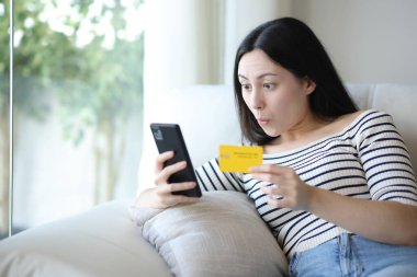 Evde telefon ve kredi kartıyla internetten satın alan Asyalı bir kadın.