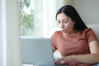 Evdeki bir kanepede oturan Asyalı kadın dizüstü bilgisayar kullanıyor.