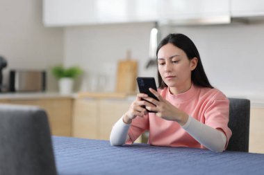 Asyalı kadın evdeki mutfakta akıllı telefon kullanıyor.