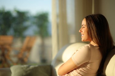 Mutlu kadın gün batımında pencereden içeri dalıp evdeki kanepede oturuyor.