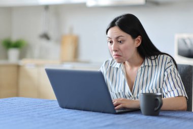 Evdeki mutfakta laptiop kullanan kafası karışmış Asyalı kadın.
