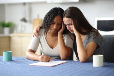 Üzücü ırklar arası lezbiyen çift evdeki mutfakta kağıt imzalıyor.