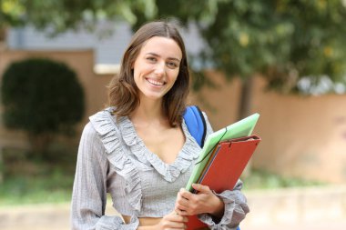 Dosyaları olan mutlu öğrenci sokakta kameraya bakıyor.