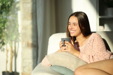 Evdeki mutlu kadın pencereden bakıp kanepede oturup kahve içiyor.