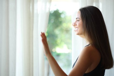 Pencereden bakan genç bir kadın. Evde duruyor.