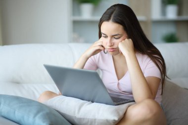 Evde kanepede dizüstü bilgisayar kullanan sıkıcı bir kadın.