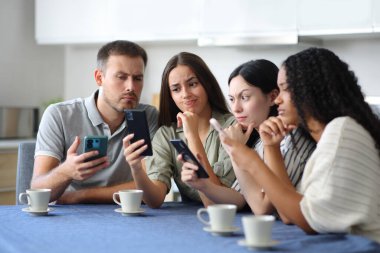 Şüpheli ırklar arası arkadaş grubu evdeki mutfakta telefonları kontrol ediyor.