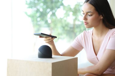 Telefonunu akıllı hoparlörle eşleştiren kadın evdeki kanepede oturuyor.