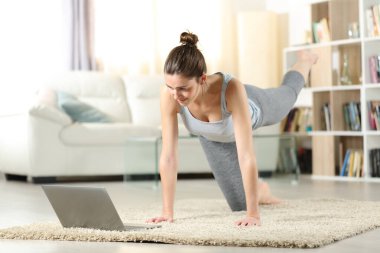 Woman at home doing exercises watching online tutorial on laptop clipart