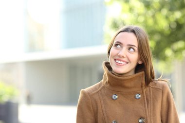 Mutlu bir kadın kışın caddede düşünürken yan tarafa bakıyor.