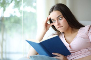 Evdeki bir kanepede oturup kitap okuyan hayret verici bir kadın.