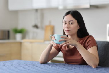 Kafası karışmış Asyalı kadın evdeki mutfakta kahve içiyor.
