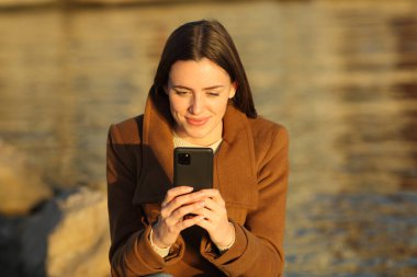 Kışın gün batımında cep telefonu kullanan rahat bir kadının portresi.