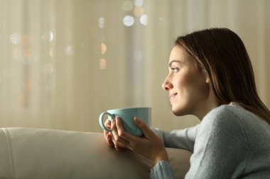Rahatlamış kadın gece evde kahve içiyor ve düşünüyor.