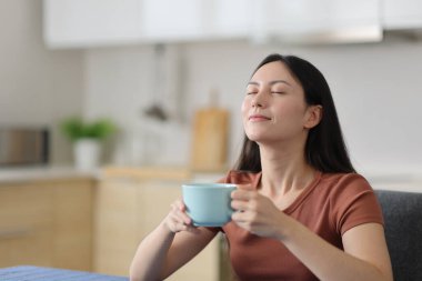 Asyalı kadın evde kahve içip nefes alıyor.