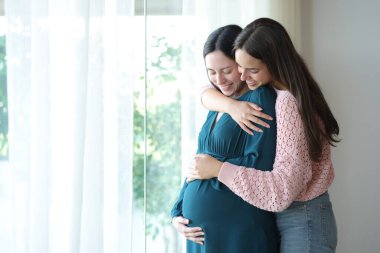 Mutlu ırklar arası lezbiyen çift, pencerede hamileliğin tadını çıkarıyor.