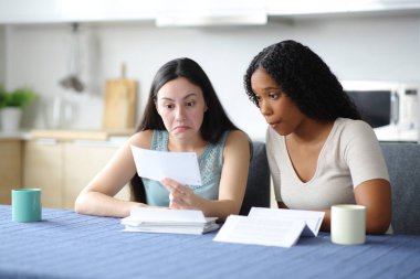 Kafası karışmış ırklar arası oda arkadaşları evdeki mutfakta kağıt banka hesaplarını kontrol ediyor.