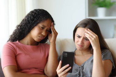 İki endişeli ırklar arası arkadaş telefonları kontrol ediyor ve evde şikayet ediyorlar.