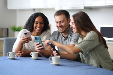 Mutlu ırklar arası arkadaşlar evdeki mutfakta akıllı telefonlarını kontrol ediyor.