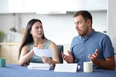 Asyalı kadın, ortağını azarlıyor. Evdeki mutfakta banka hesap özetini tutuyor.