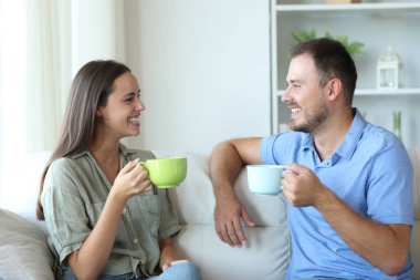 Mutlu çift evde konuşuyor. Kanepede oturup içiyorlar.