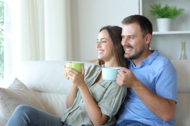 Mutlu çift pencereden bakıyor ve evdeki kanepede oturup kahve içiyor.