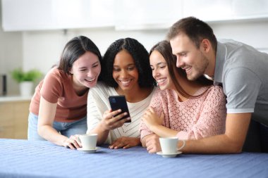 Mutlu ırklar arası arkadaş grupları evdeki mutfakta telefonları kontrol ediyor.
