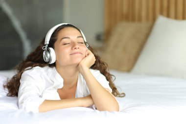 Yatağa uzanmış, kablosuz kulaklıkla ses dinleyen rahat bir kadın.