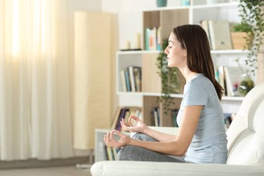 Evde yoga yapan, kanepede oturan bir kadının yan görüntüsü.