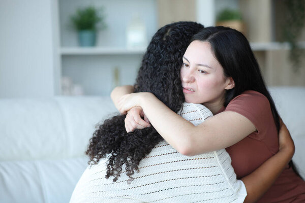 False asian woman hugging her friend sitting on a couch at home