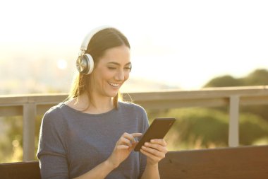 Kulaklık takan mutlu kadın dışarıda telefonla müzik dinliyor.