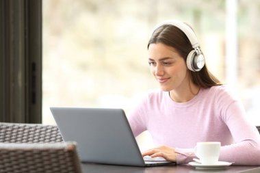 Restoranda laptop ve kulaklık kullanarak medyayı izleyen rahat bir kadın.
