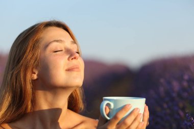 Lavanta tarlasında temiz hava soluyan kadın gün batımında çay içiyor.