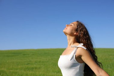 Beyaz elbiseli kadın yeşil alanda temiz hava soluyor. Doğada güneşli bir gün.