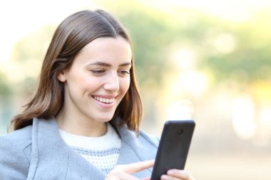 Kışın parkta cep telefonu kullanan mutlu bir kadın.