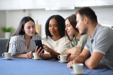 Ciddi ırklar arası arkadaşlar evdeki mutfakta cep telefonlarını kontrol ediyorlar.