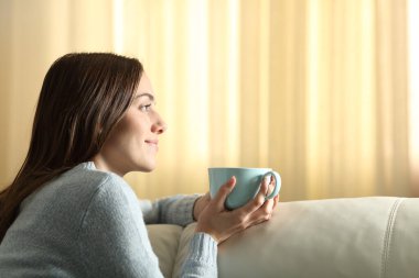 Çay içen ve evdeki kanepede oturan bir kadın.