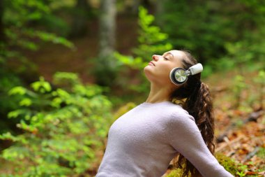 Ormanda dinlenen ve kulaklıkla ses dinleyen bir kadının profili