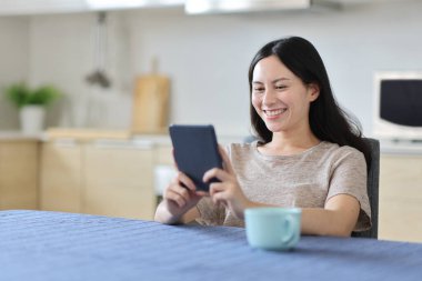 Kahvaltıda evde, mutfakta kitap okuyan mutlu Asyalı kadın.