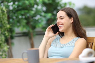 Mutlu kadın terasta oturmuş telefonda konuşuyor.