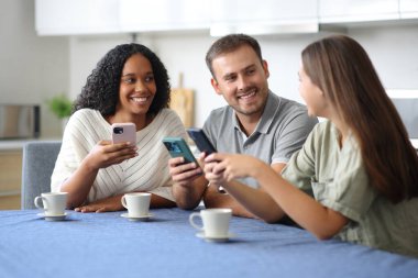 Üç ırklar arası arkadaş akıllı telefonlarını kontrol edip evde konuşuyorlar.