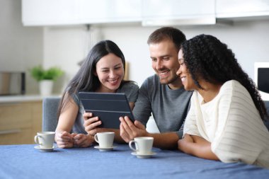 Mutlu ırklar arası oda arkadaşları evdeki mutfakta tabletle medyayı izliyor.