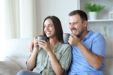 Mutlu çift gülüyor ve kahve içiyor. Evdeki bir kanepede oturuyor.