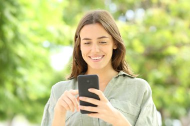 Parkta cep telefonuyla yürüyen bir kadının portresi.