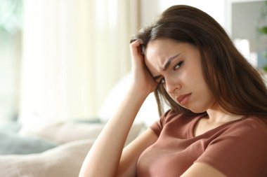 Evdeki kanepede oturan kızgın kadın kameraya bakıyor.