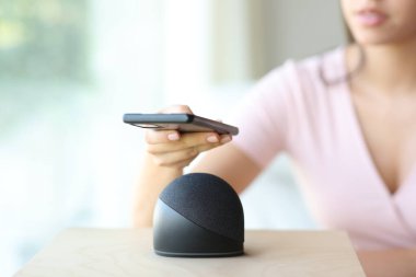 Evde akıllı hoparlörle cep telefonu eşleştiren bir kadının fotoğrafını çek.